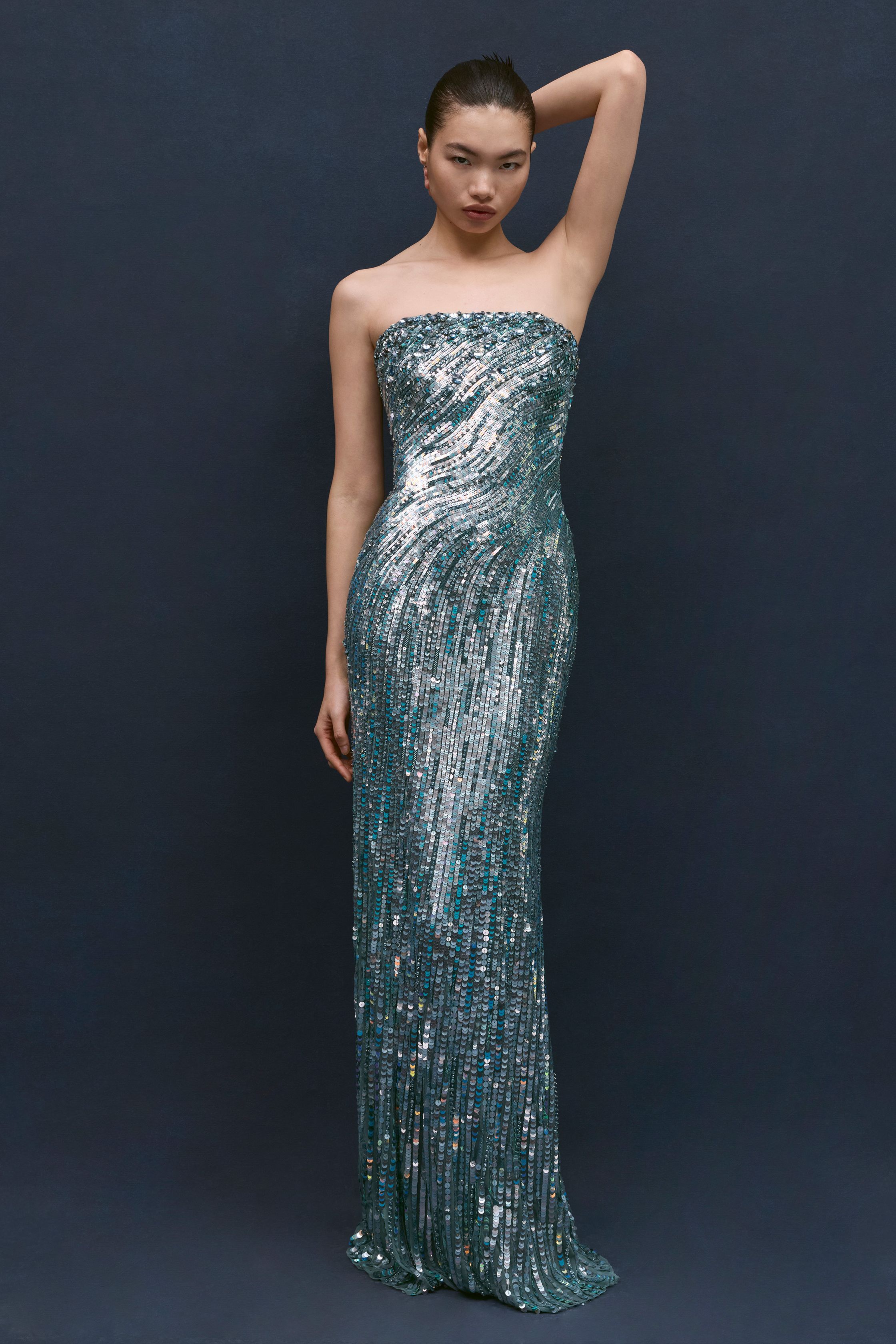 Jenny Packham本季延续品牌标志性的红毯礼服风格，以闪耀流苏、金属光泽与修身长裙构建极具戏剧感的夜晚造型。银色亮片与深蓝礼服形成冷艳优雅的视觉对比，垂坠流苏与贴身剪裁让服装在行走间呈现波光般的流动感。设计在极简轮廓中加入华丽装饰，使整个系列既保留经典好莱坞 glamour，又展现现代女性的自信与优雅-顽石频道趋势研究